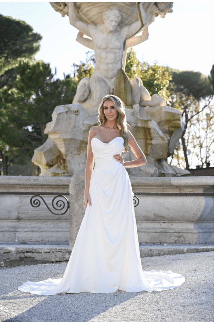 IVORY – Strapless, plain soft satin A-line with draped detail on front bodice & skirt. Gathered back skirt with pearl button trim & optional large detachable bow with tail included unless ordering dress only.